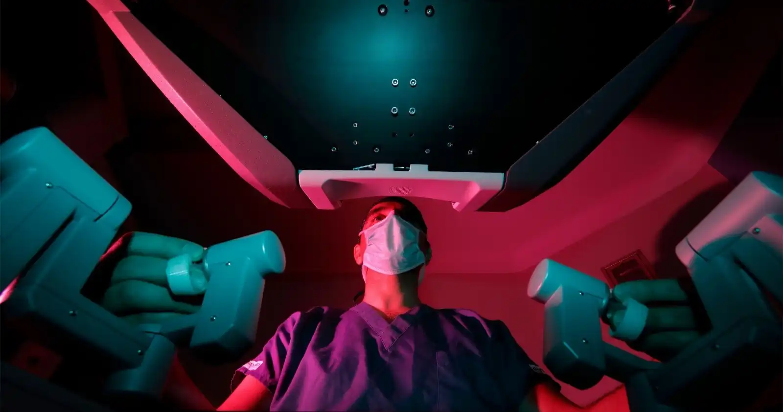 Surgeon operating a robotic surgical system viewed from below with dramatic teal and pink lighting, representing advanced medical technology in accredited Turkish hospitals